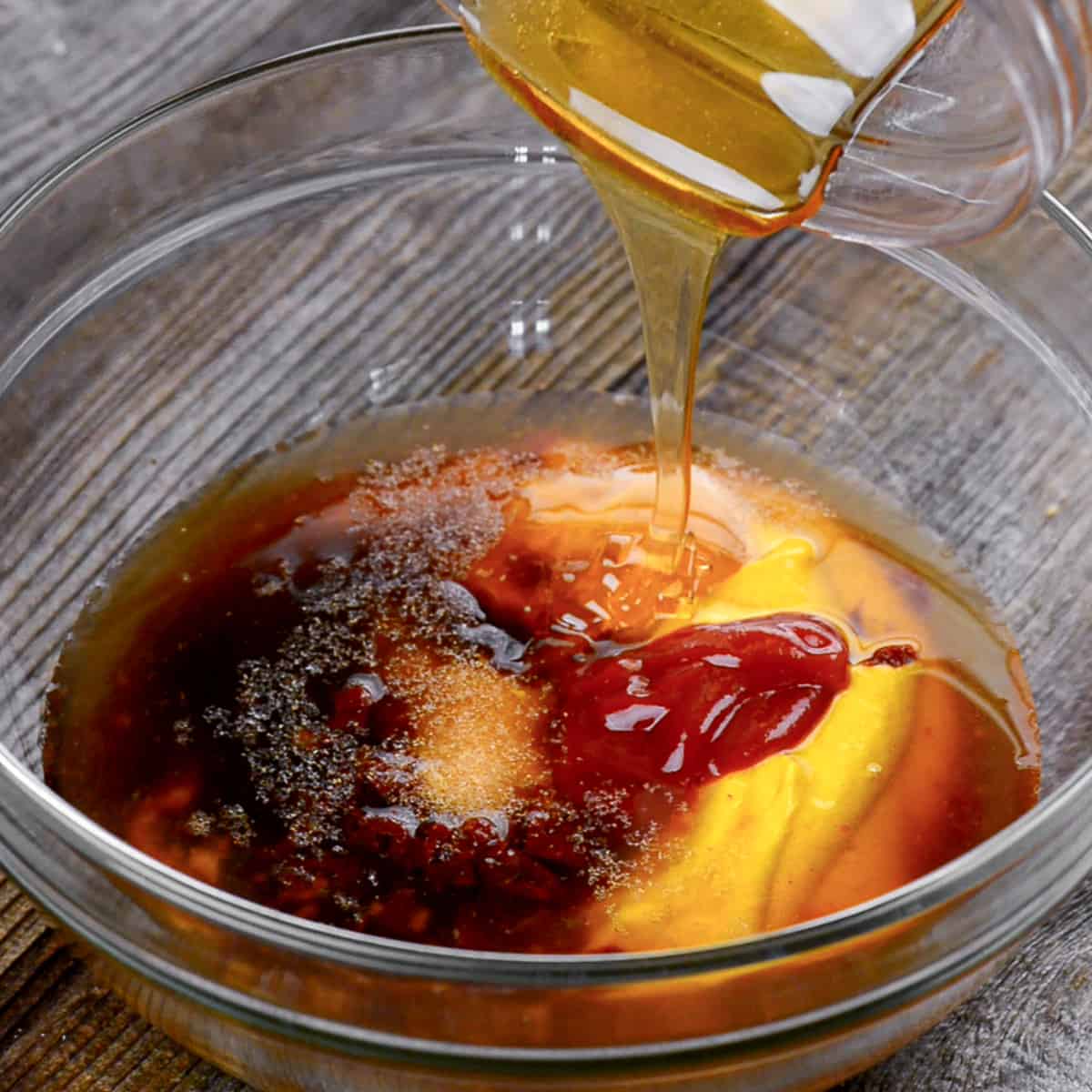 Adding honey to Carolina mustard bbq sauce ingredients in glass bowl.