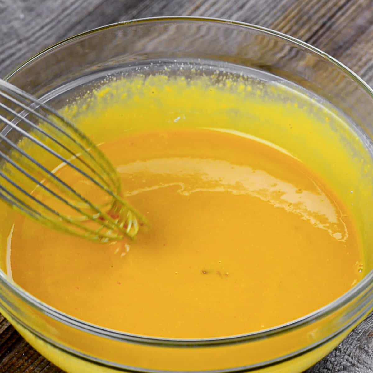 Mixing Carolina mustard bbq sauce with whisk in glass bowl.
