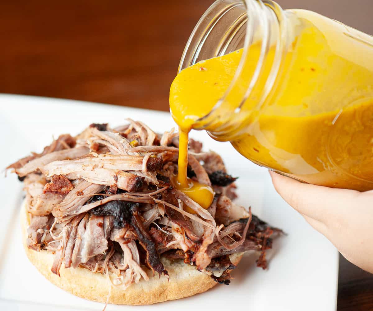 Pouring Carolina mustard bbq sauce onto smoked pulled pork sandwich.