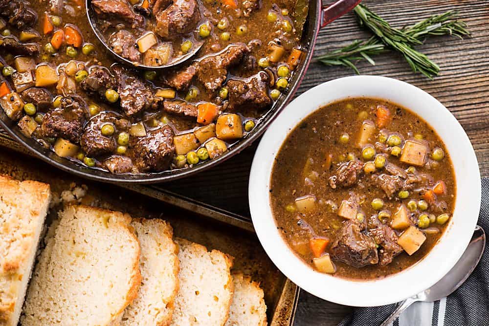 bowl of beef stew next to pot with sliced bread