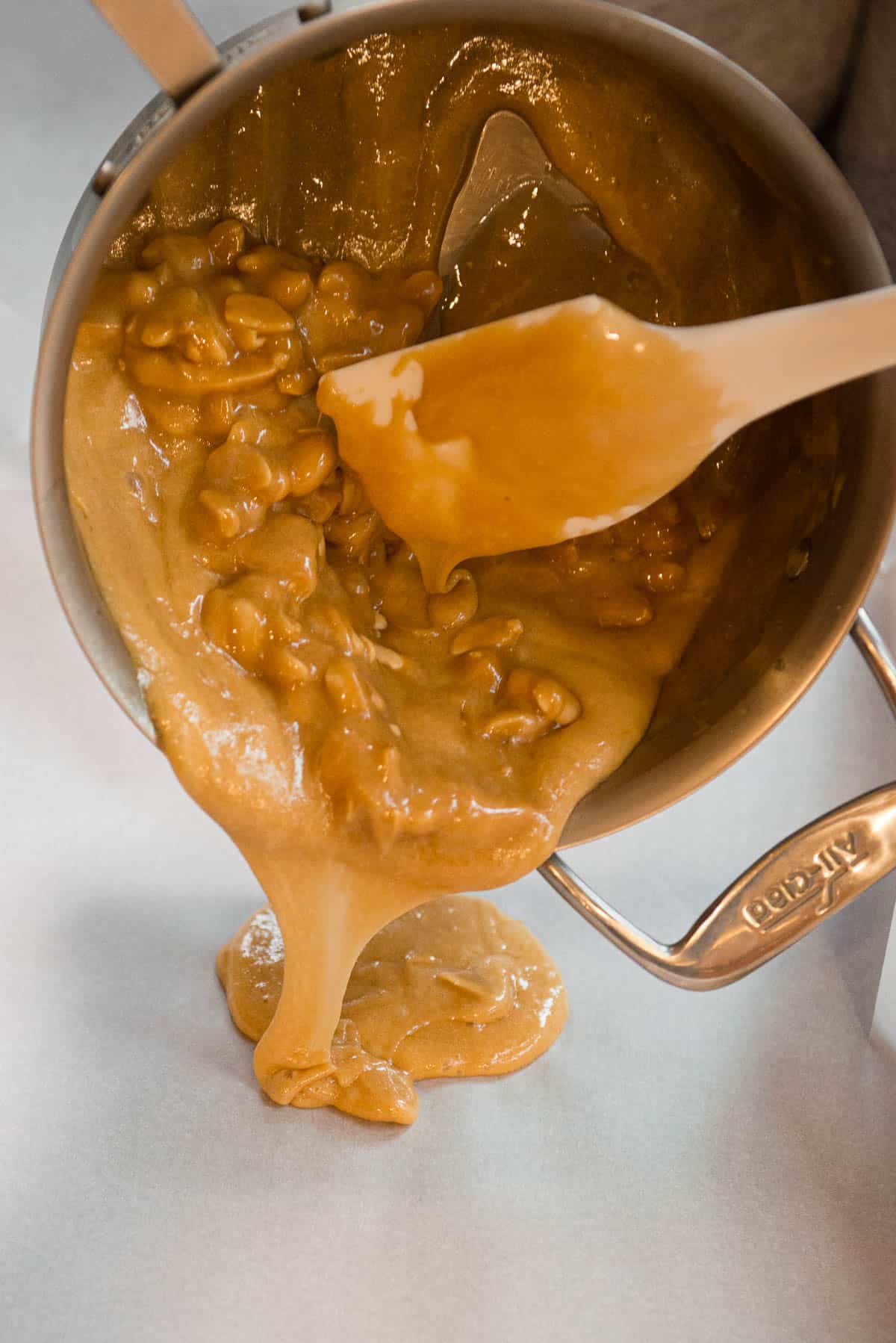 pouring hot peanut brittle from pan onto parchment paper