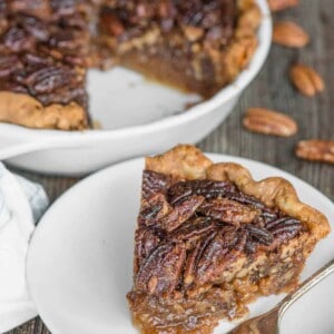 slice of pecan pie on white plate with pie behind it