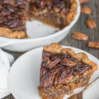 slice of pecan pie on white plate with pie behind it