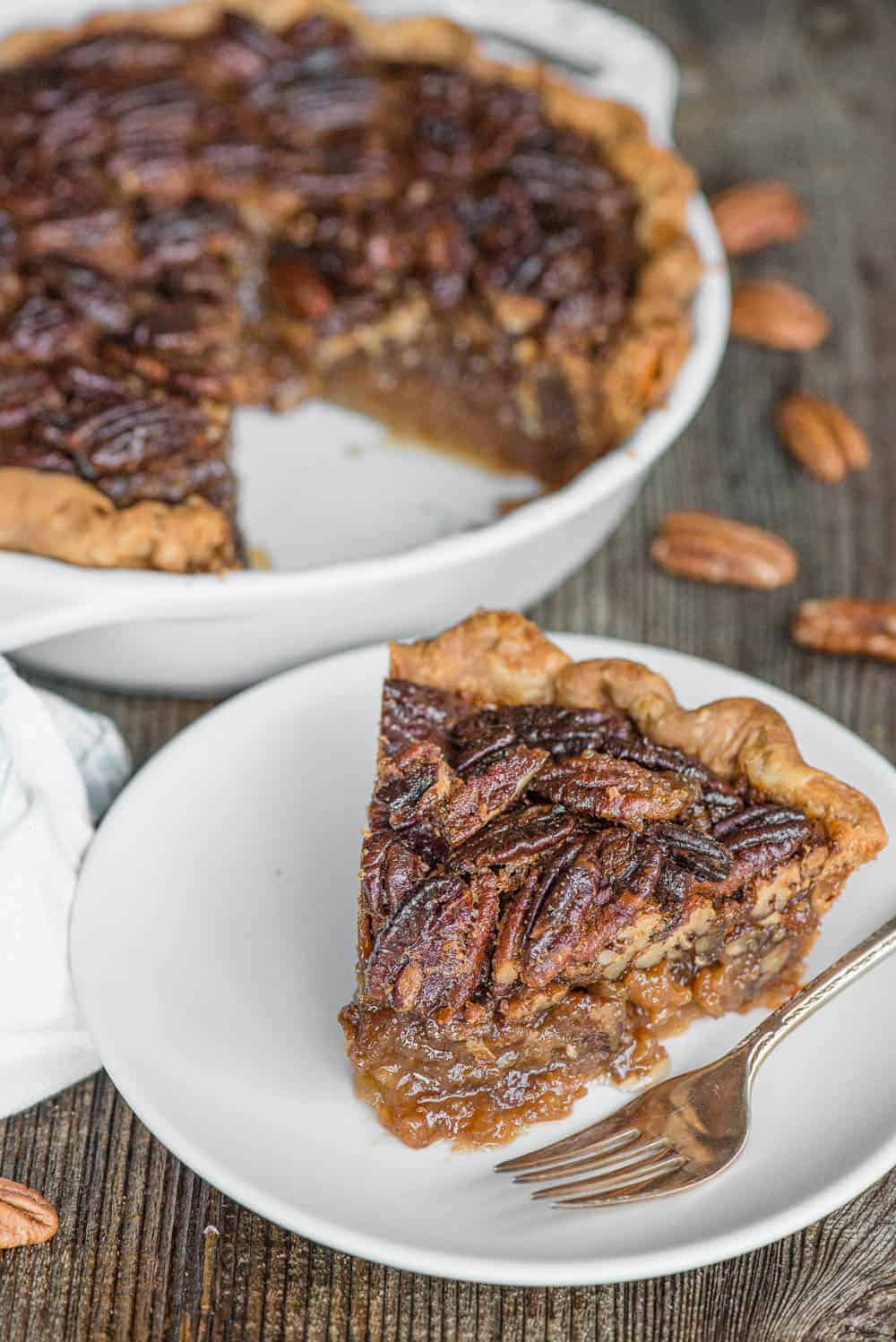 slice of pecan pie on white plate with pie behind it