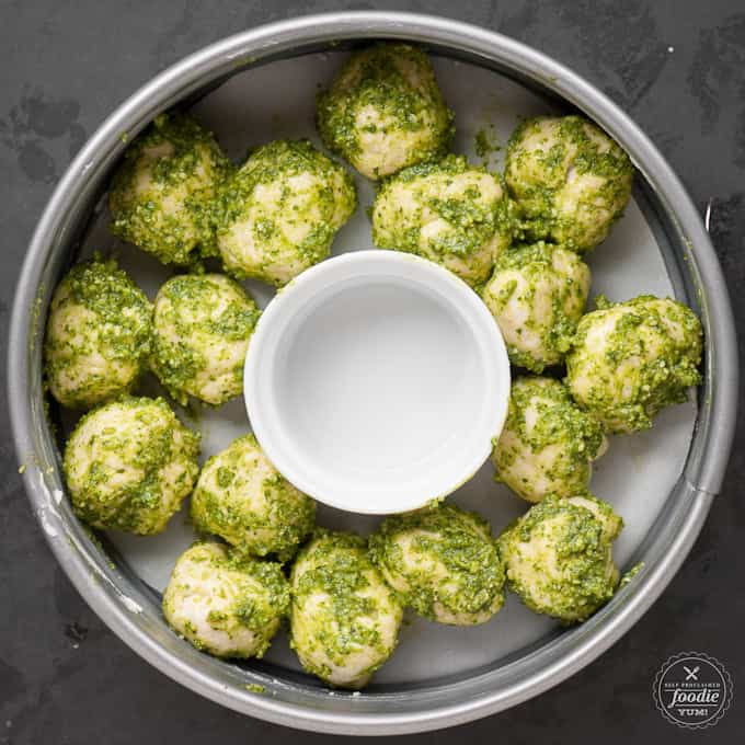uncooked pesto cheese bombs in round pan with ramekin in middle