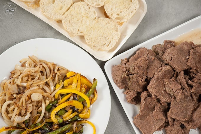 three plates with peppers and onions, sliced cooked beef, split rolls