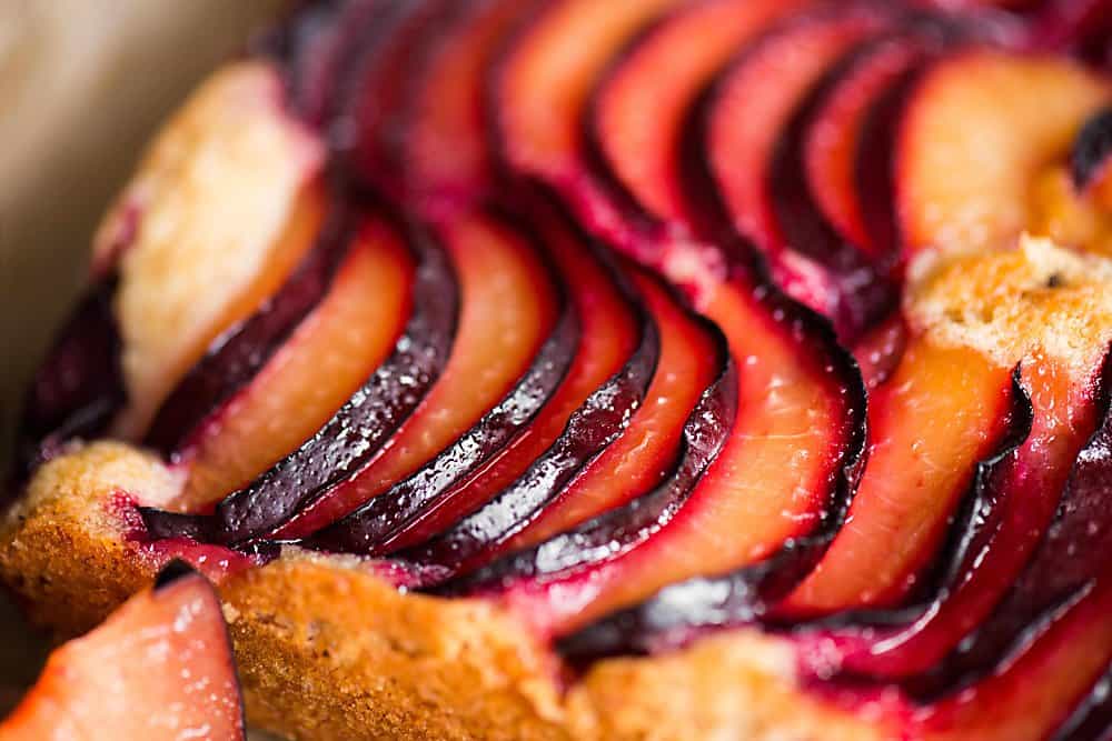 A close up of thin plum slices on top of cake