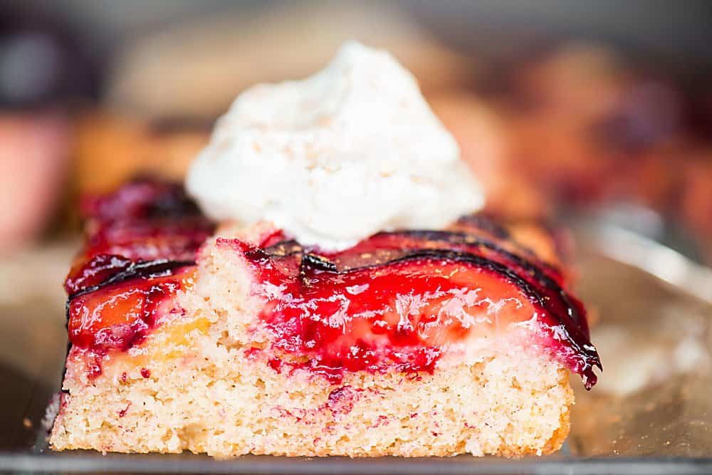 A close up of a piece of cake on a plate, with plums and Whipped cream