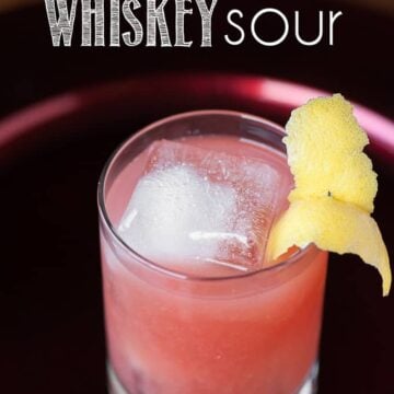 A glass of pomegranate Whiskey sour with lemon garnish