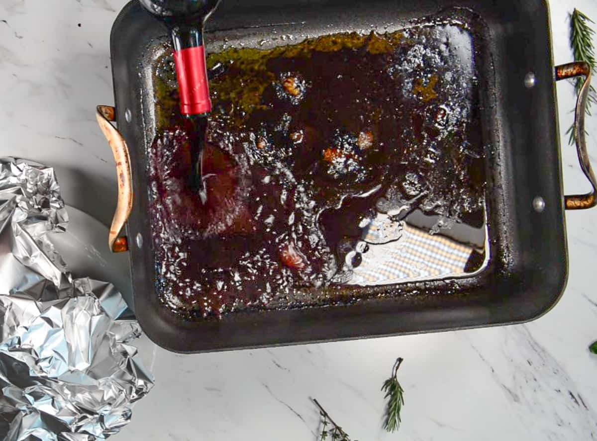 Pouring red wine into roasting pan with prime rib roast drippings.