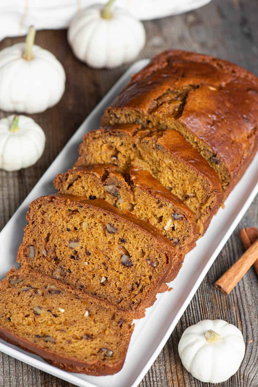 sliced homemade pumpkin bread on white platter with white pumpkin decorations