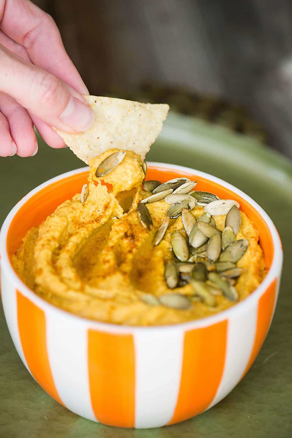 a tortilla chip being dipped in pumpkin curry hummus