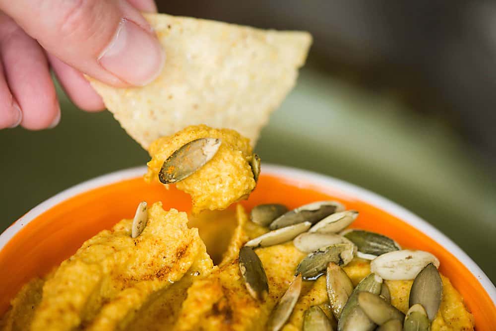 A close up of a tortilla chip dipped in pumpkin curry hummus