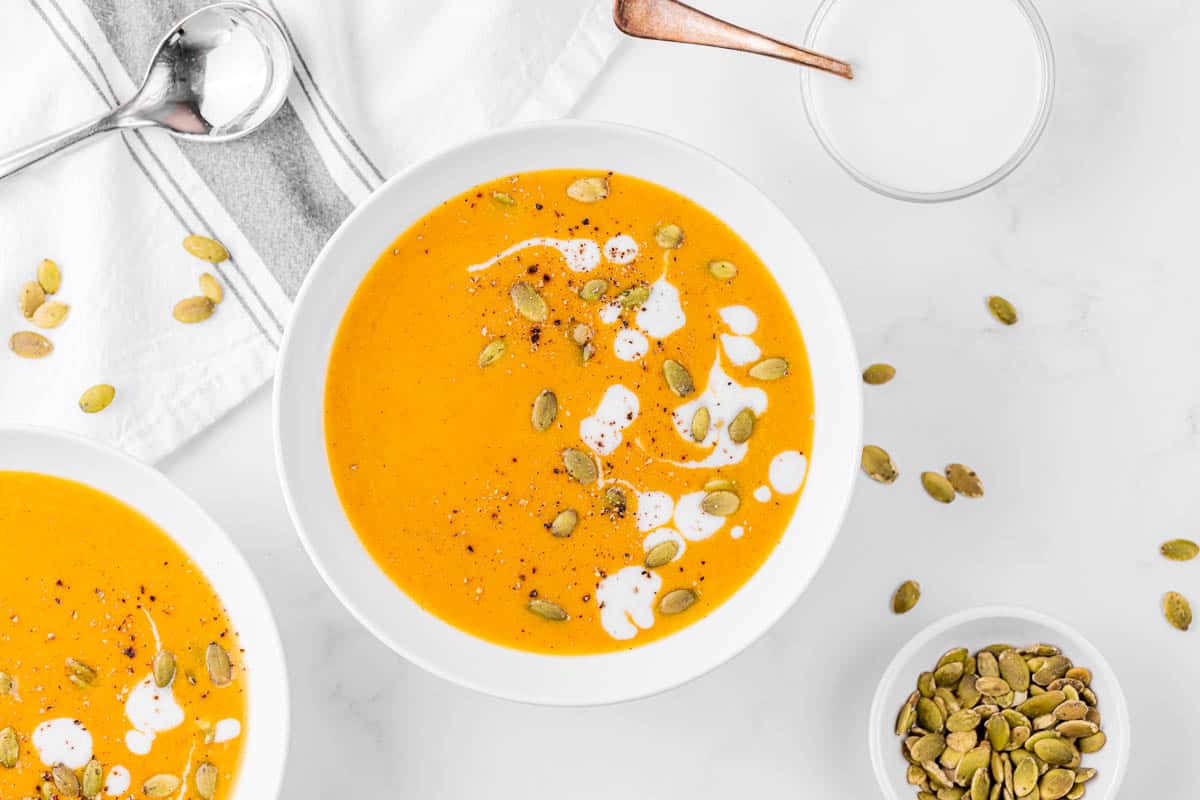 Bowl of pumpkin curry soup in white bowl garnished with heavy cream and pumpkin seeds.