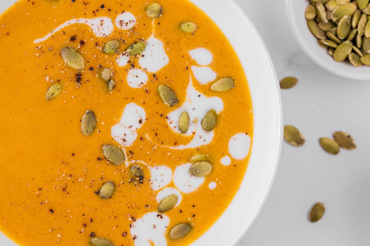 Bowl of pumpkin curry soup in white bowl garnished with heavy cream and pumpkin seeds.
