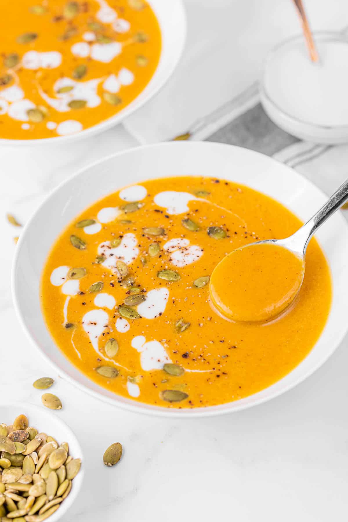 Bowl of pumpkin curry soup in white bowl garnished with heavy cream and pumpkin seeds.