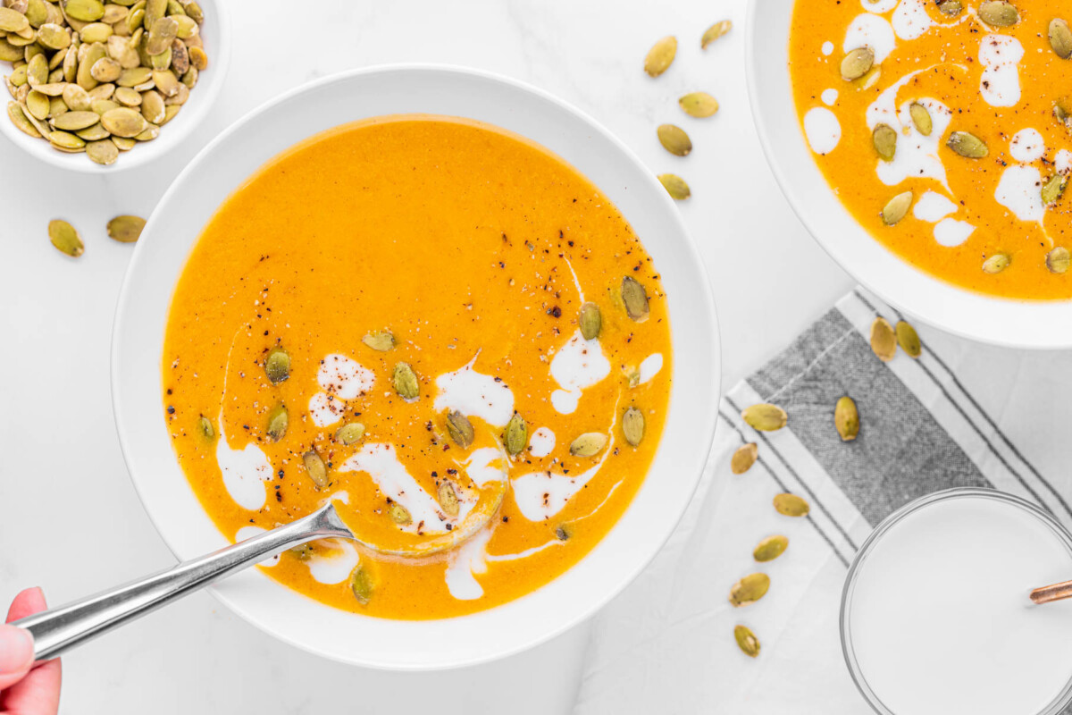 Bowl of pumpkin curry soup in white bowl garnished with heavy cream and pumpkin seeds.