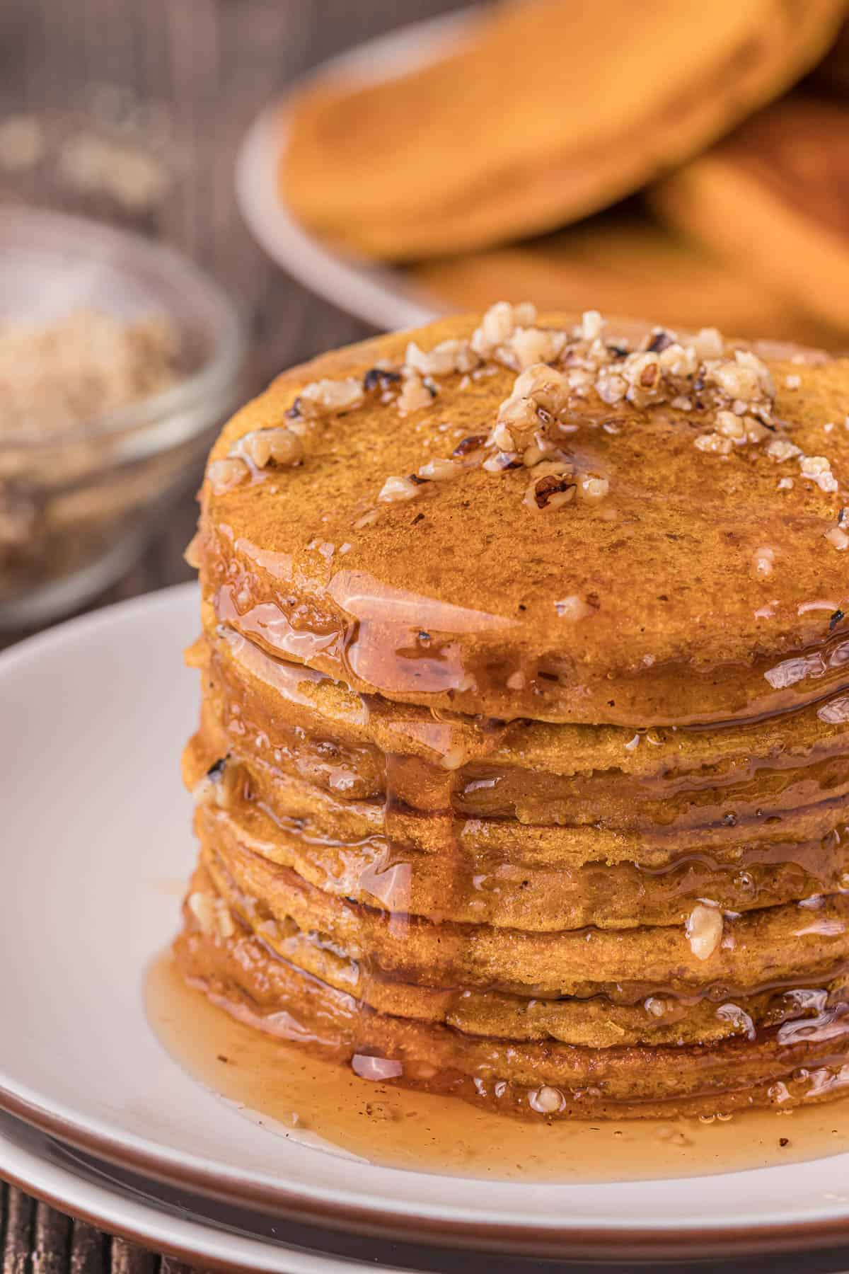 tall stack of pumpkin pancakes with crushed nuts and syrup.