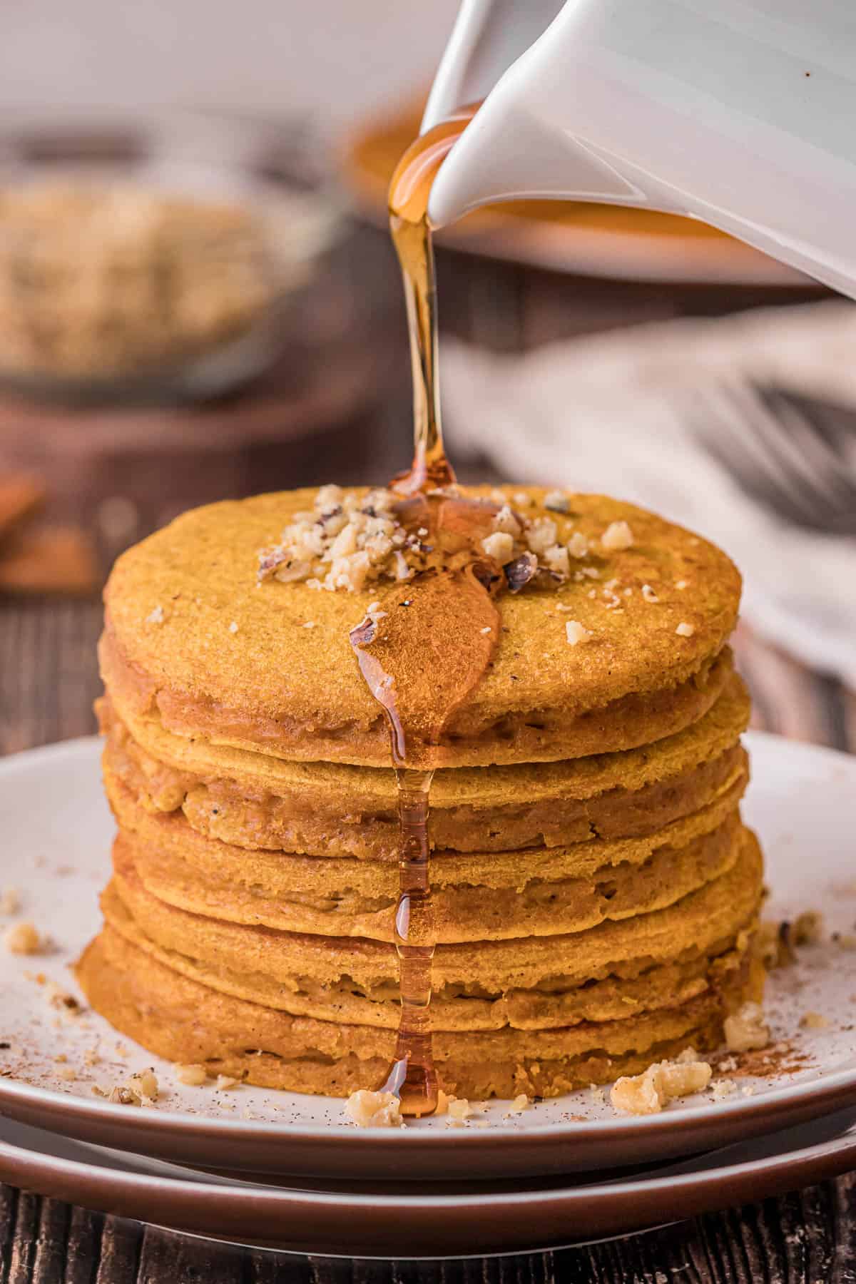 pouring syrup on stack of homemade pumpkin pancakes.