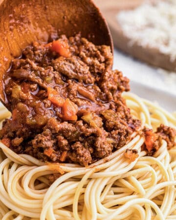 spooning homemade beef ragu sauce onto spaghetti noodles.
