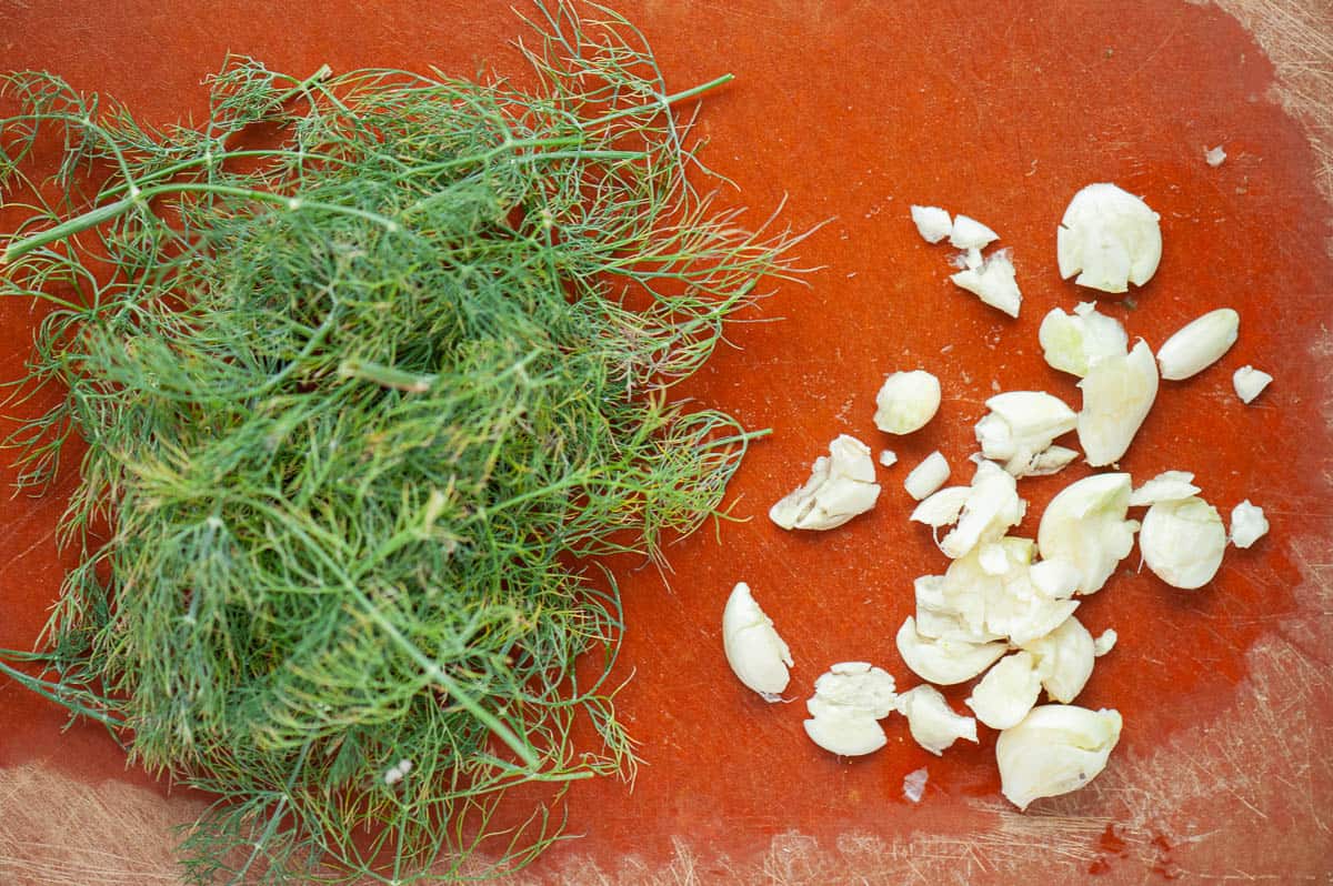 smashed fresh garlic and fresh dill on cutting board.