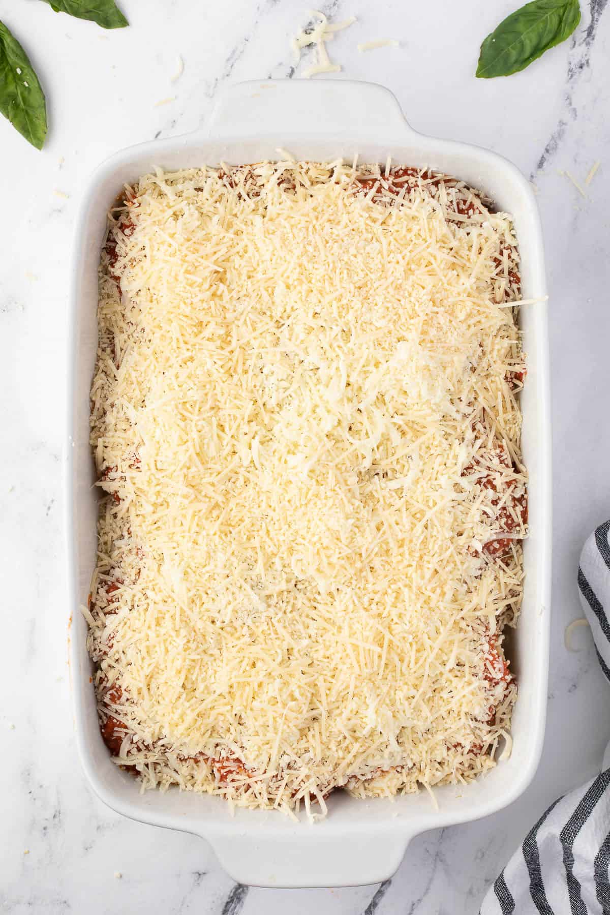 shredded cheese over marinara sauce in casserole dish