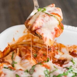 scooping homemade ricotta stuffed shells out of baking dish