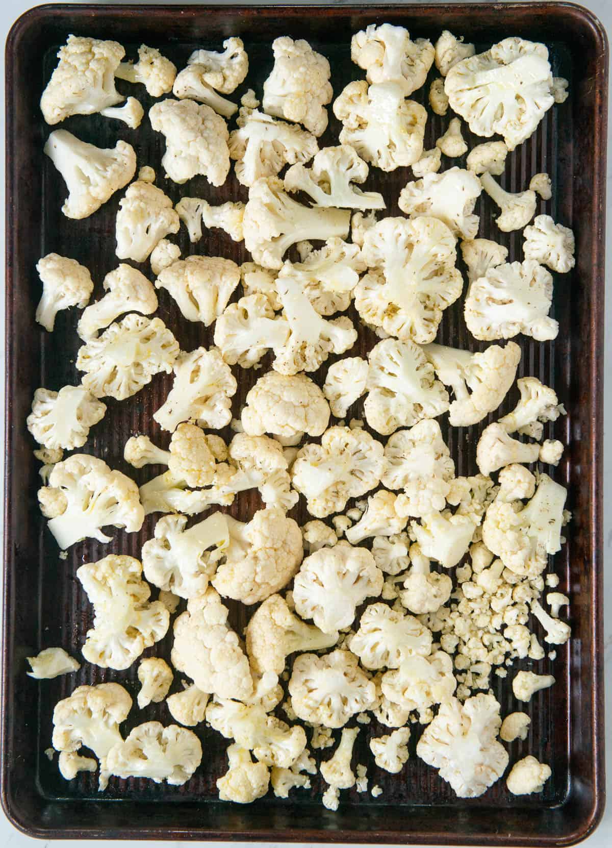 raw cauliflower florets with olive oil on baking sheet.