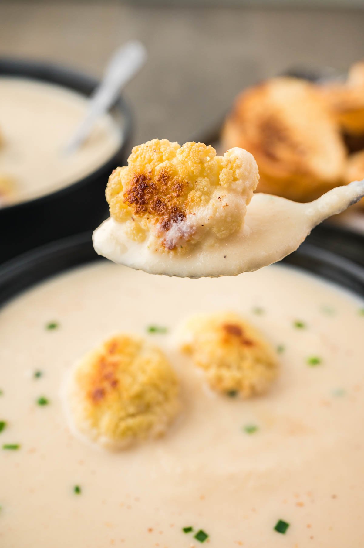 spoonful of roasted cauliflower soup with a piece of roasted cauliflower.