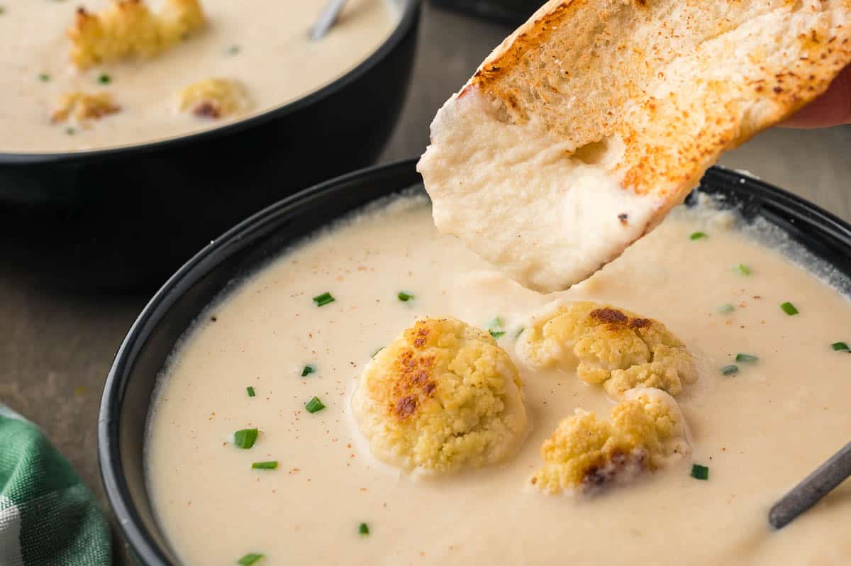 dipping toast into bowl of roasted cauliflower soup.