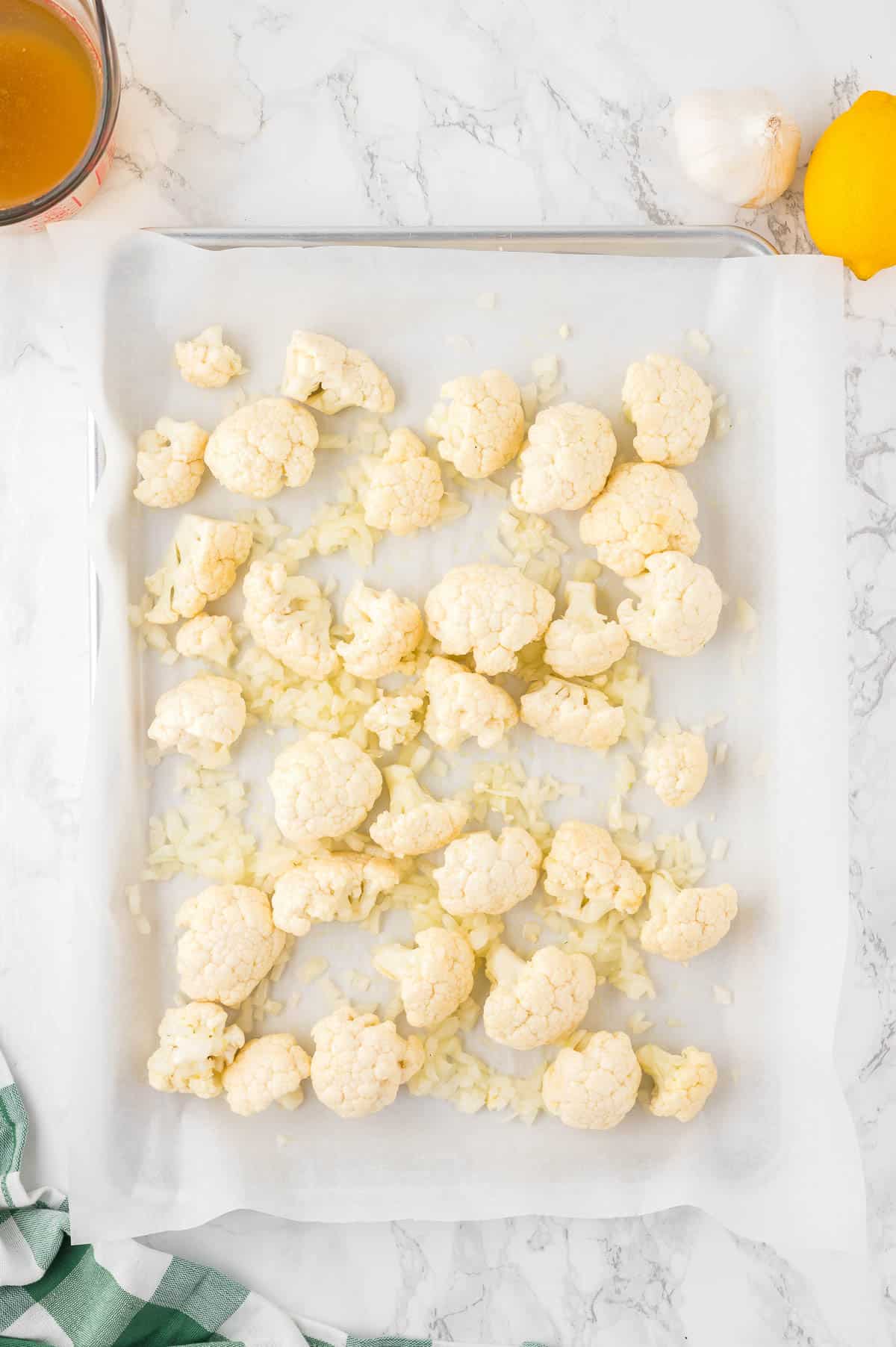 cauliflower and onion on parchment lined baking sheet.
