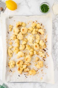 roasted cauliflower and onion pieces on parchment lined baking sheet.