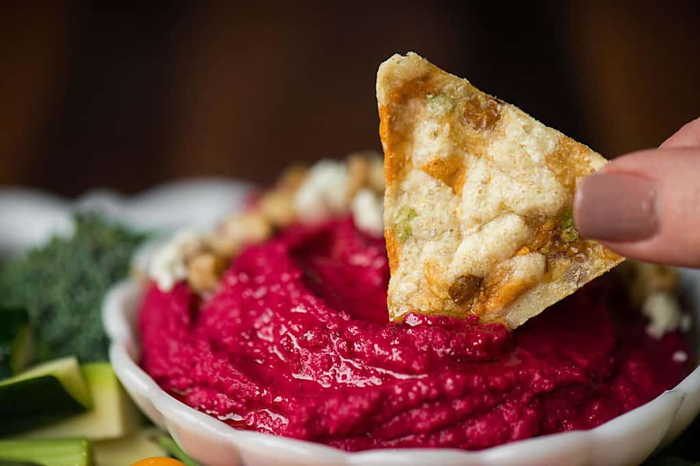 roasted garlic beet hummus with a tortilla chip dipped in it