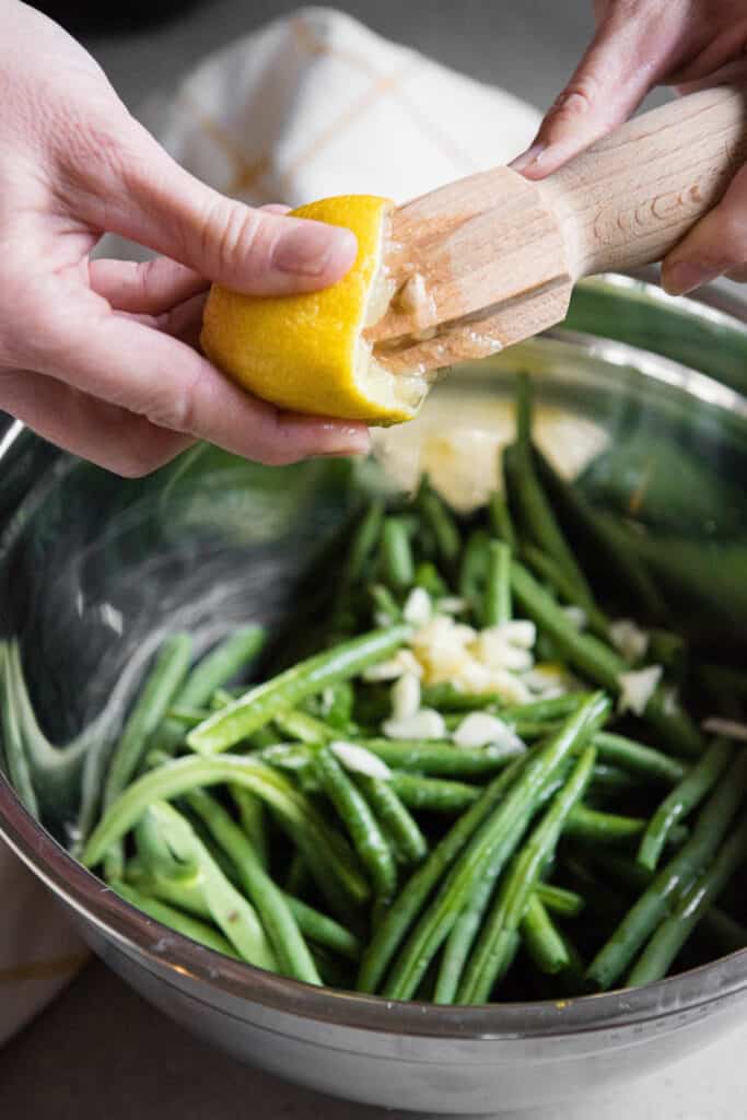 squeezing lemon over blanched green beans with garlic.