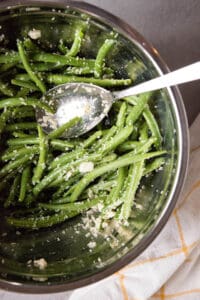 mixing green beans with parmesan and garlic in bowl.