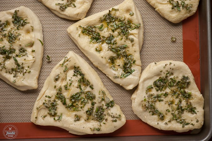 flatbread dough with herb topping on baking sheet