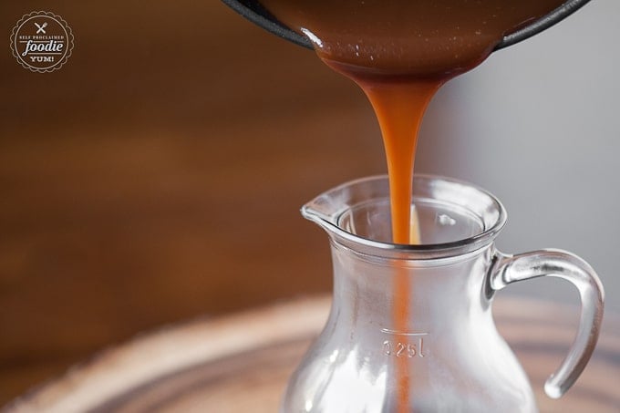 pouring homemade caramel sauce from pan into glass container