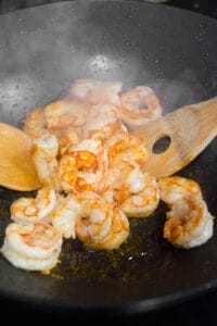 cooking shrimp in wok with wooden spoons