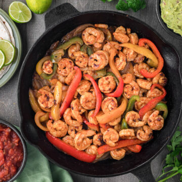 cast iron pan of shrimp fajitas with toppings.