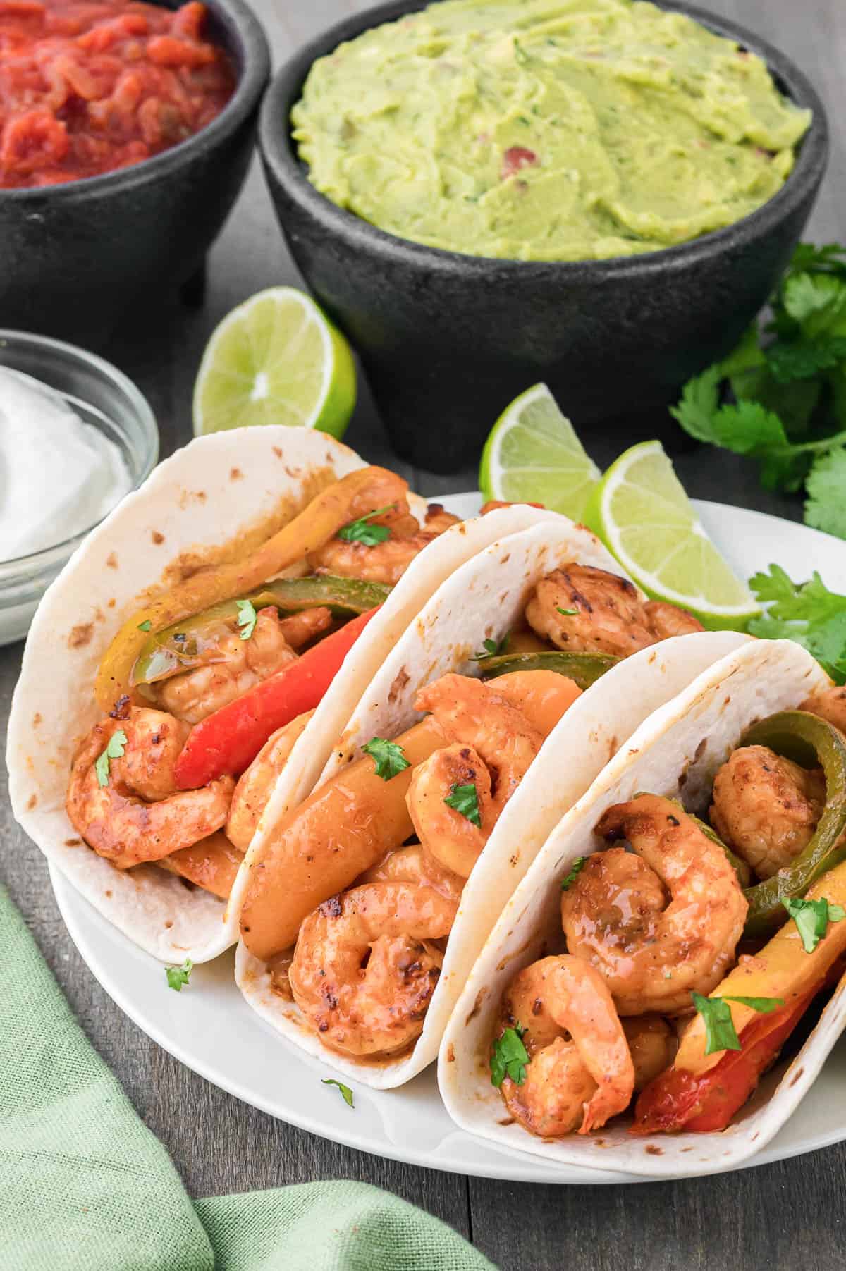 plate with shrimp fajitas in tortillas with guacamole and lime.