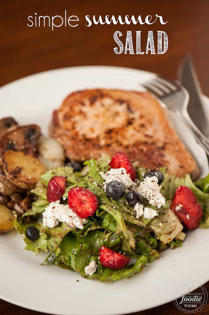 green salad with goat cheese and berries on plate with pork chop and potatoes