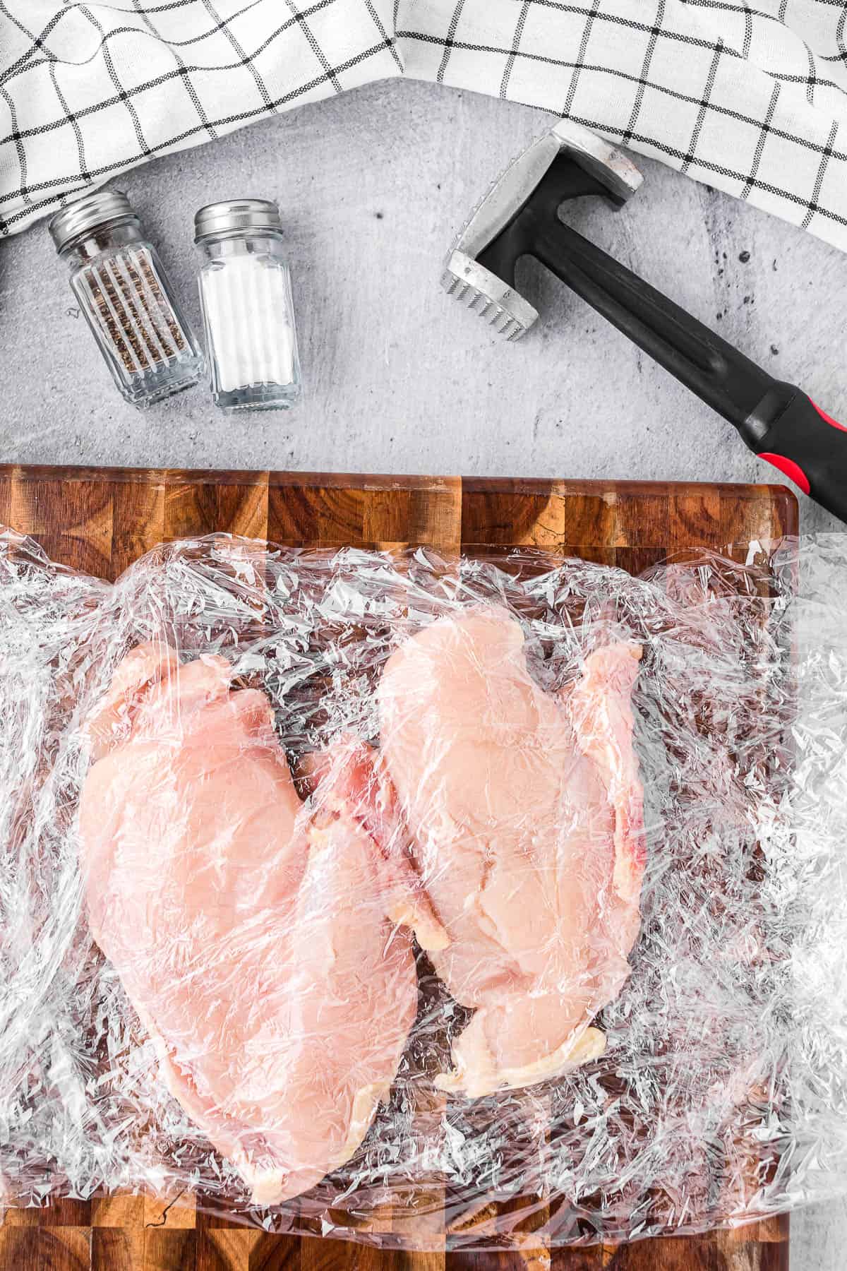chicken breasts in between plastic wrap on cutting board.