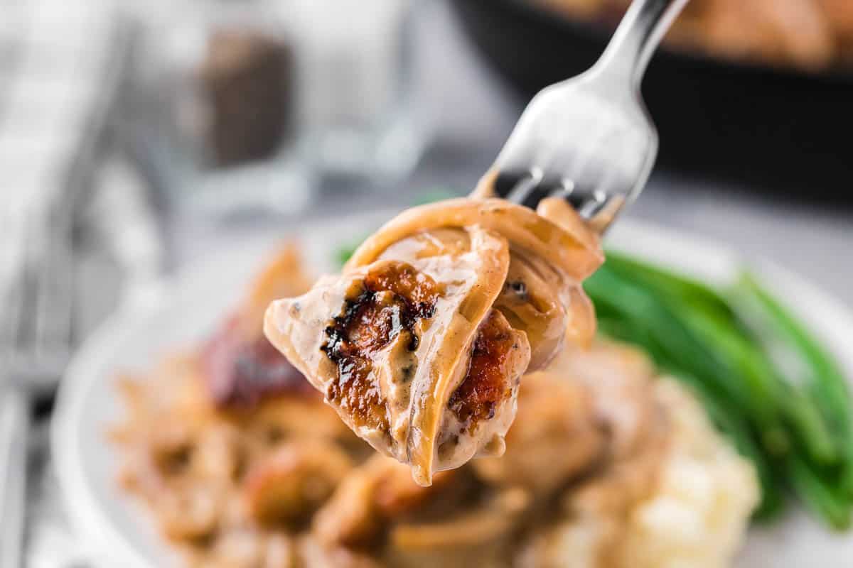 smothered chicken breasts in creamy onion gravy on fork.