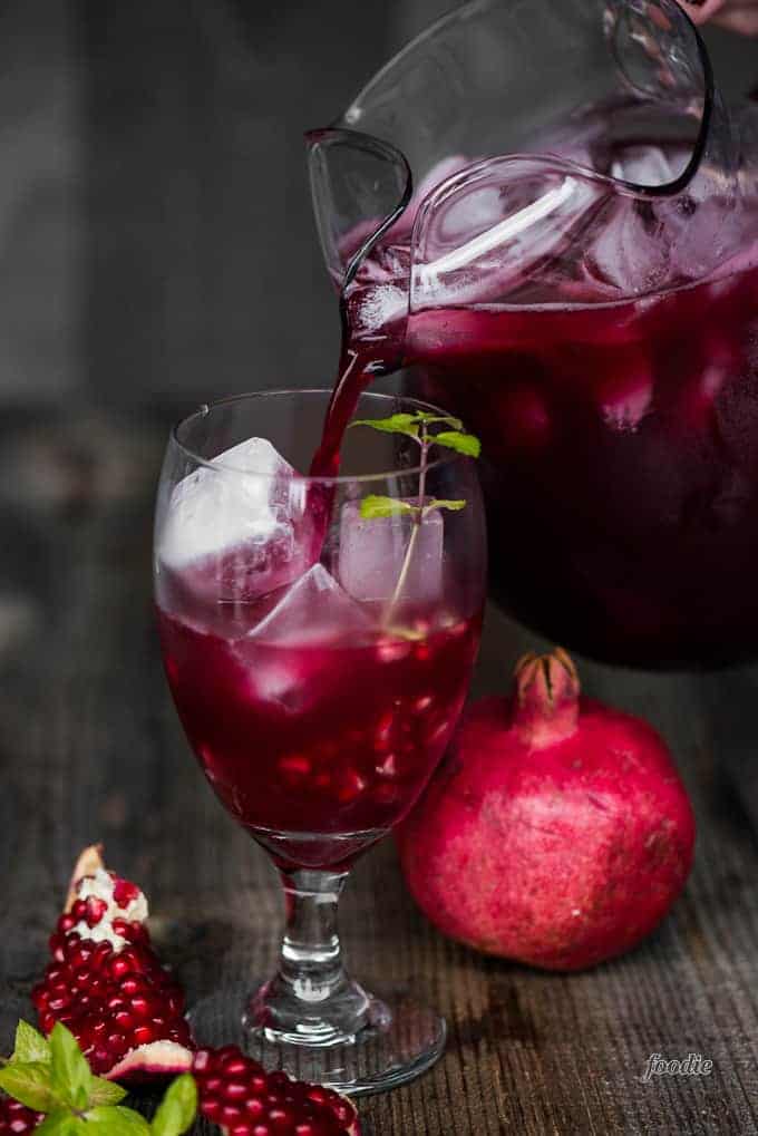 pitcher of pomegranate cocktail pouring into glass