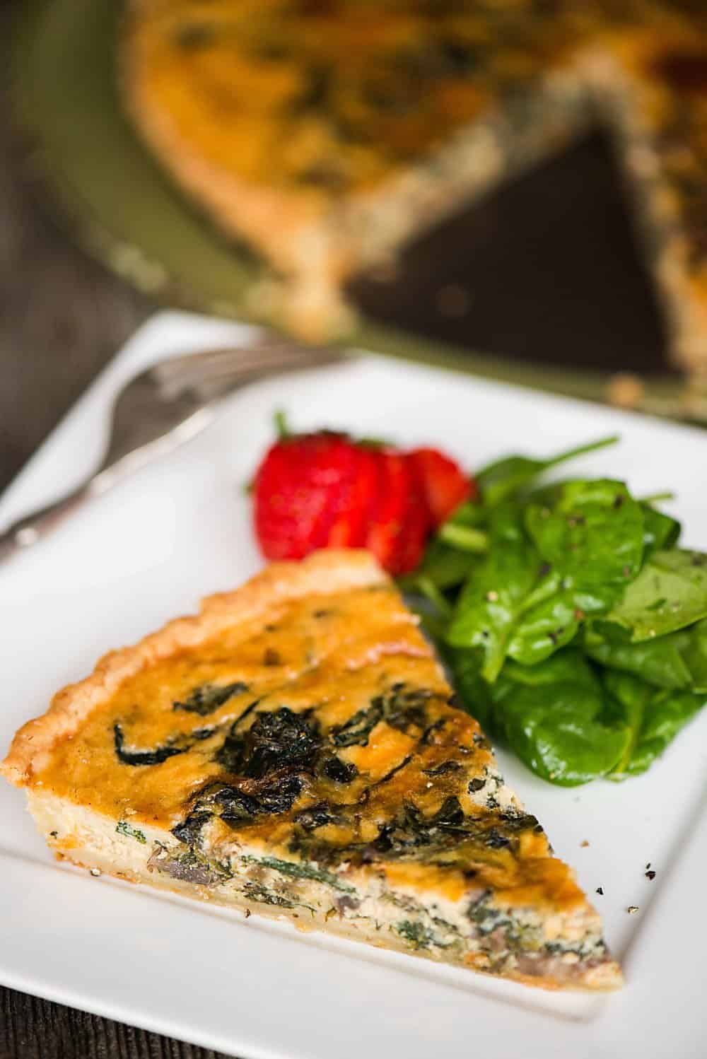 slice of homemade quiche on plate with spinach