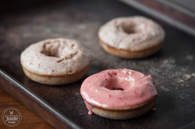 baked donuts on baking sheet, one covered in strawberry glaze