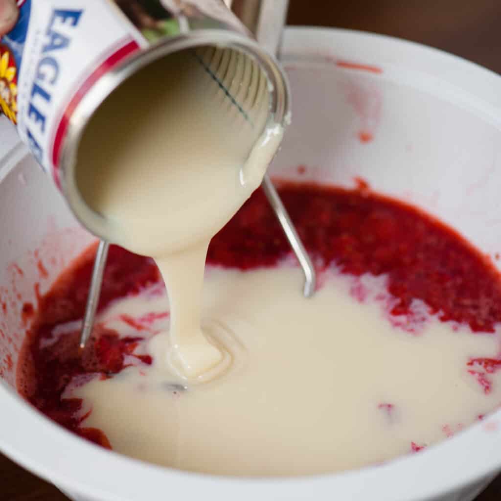 adding sweetened condensed milk to strawberries