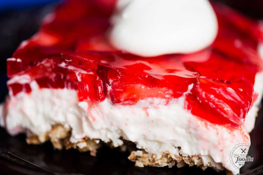 Strawberry Pretzel Dessert is the ultimate summer dessert, especially when you're looking for something sweet to take to potlucks! This tasty treat consists of a sweet pretzel crust, topped by a creamy layer, and finished off with a layer of fresh strawberries set in strawberry jello. Slice of Strawberry Pretzel Salad