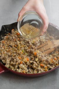 pouring white wine into sausage and rice mixture