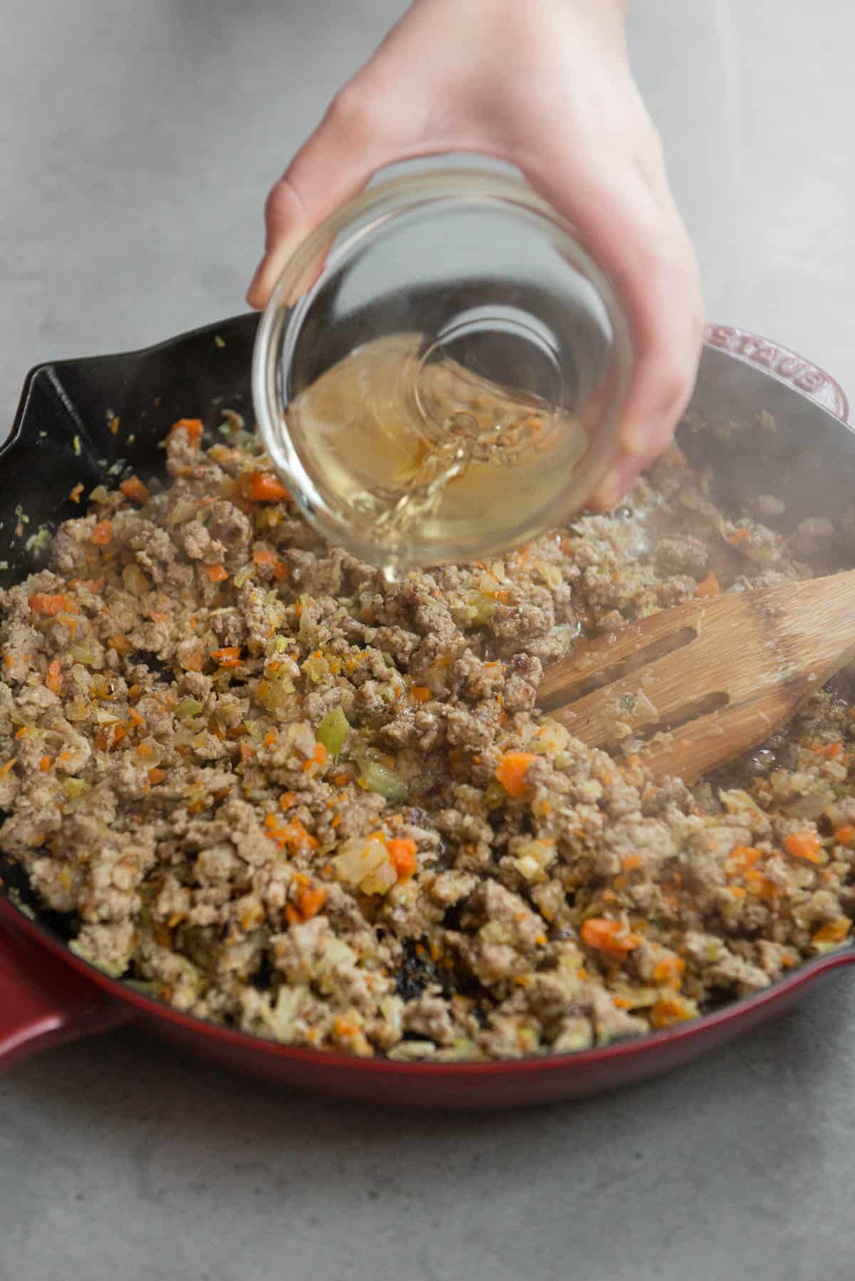 pouring white wine into sausage and rice mixture
